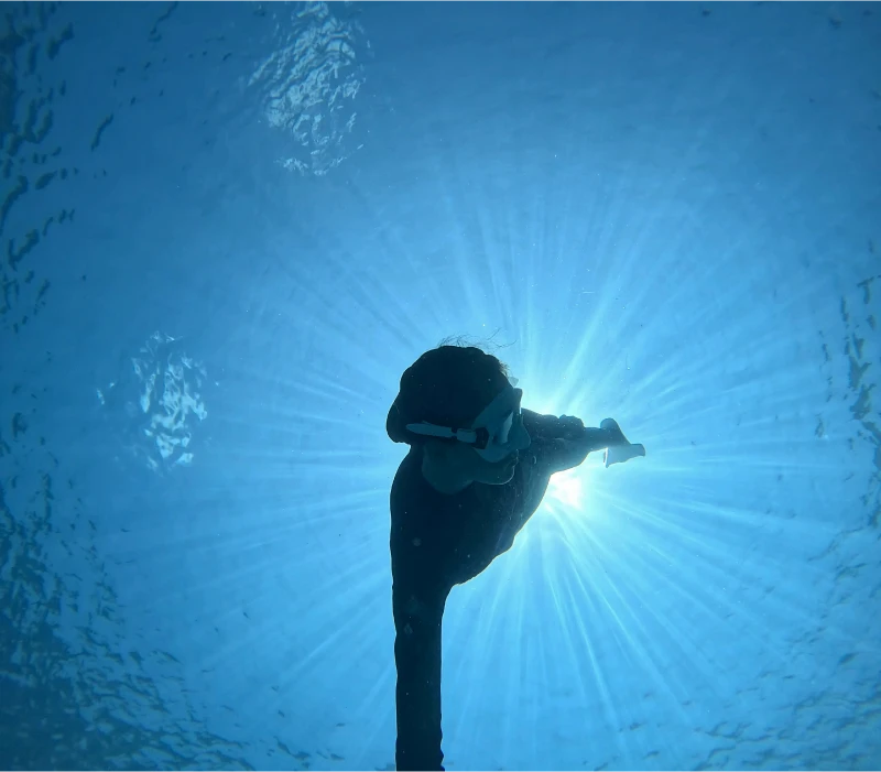 A snorkeler diving in sunlit underwater scenery