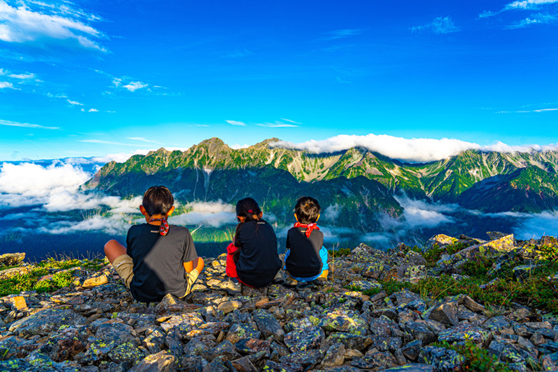 Three children gazing at distant mountains from a mountain summit