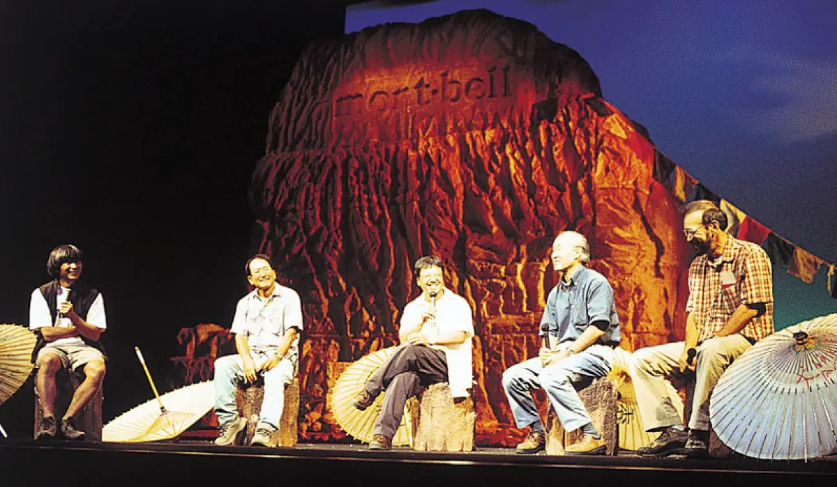Scene from a stage event at "Montbell Indoor Challenge." Five men sitting on chairs participating in a talk show.