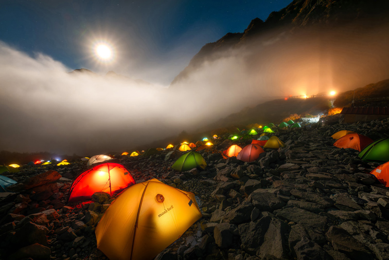 Under the moonlight and a sea of clouds, numerous tents illuminated with light