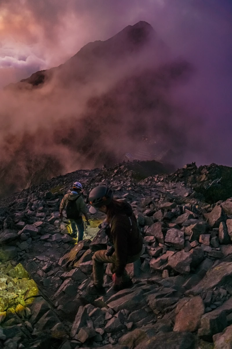 Two climbers are descending a rocky area, illuminating their path with headlamps.