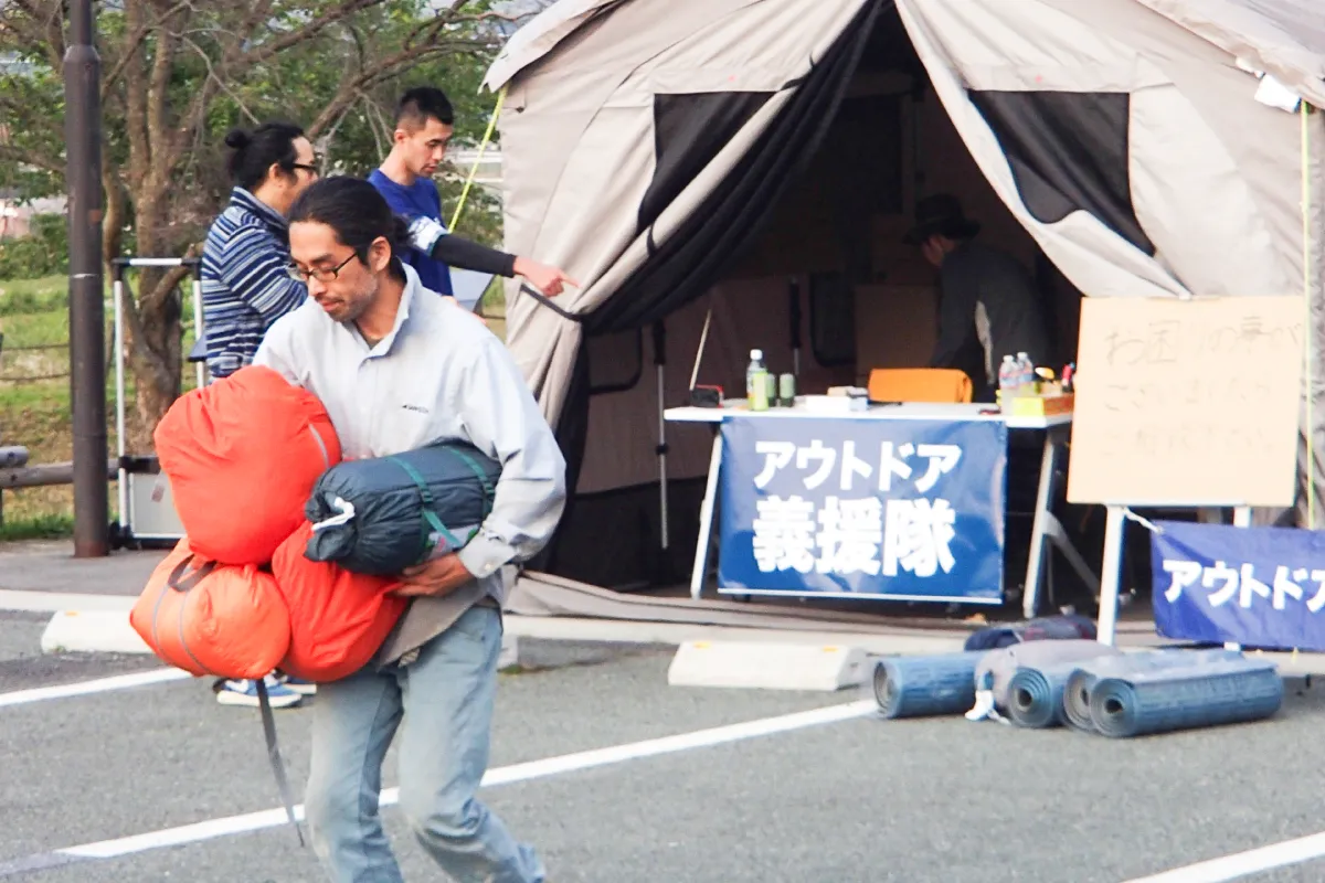 A man is receiving a tent as relief supplies from the tent set up by the Outdoor Gientai as their base of operations