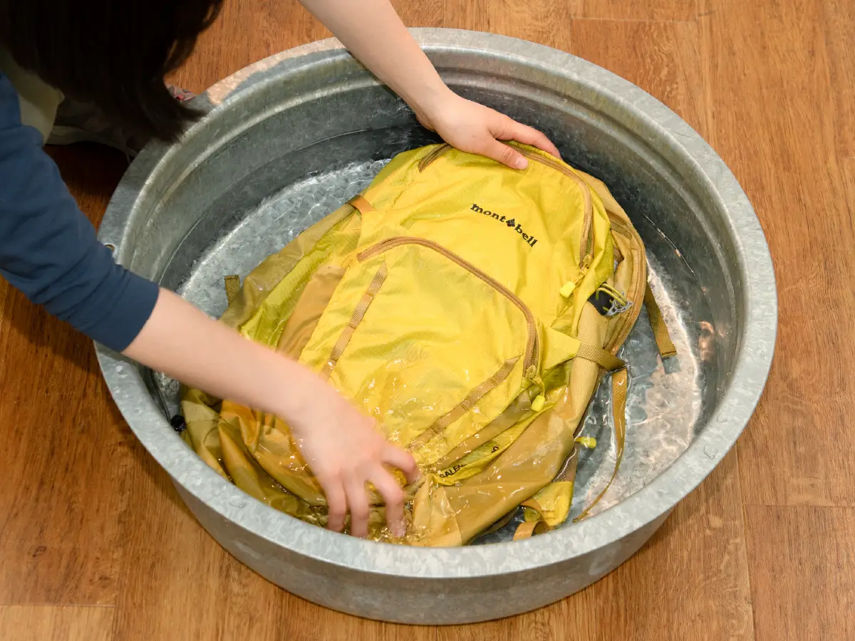 Photo of a backpack being placed in a tub of water and rinsed.