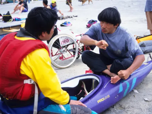 Isamu Tatsuno demonstrates kayaking techniques and teaches paddling to a wheelchair user with a disability