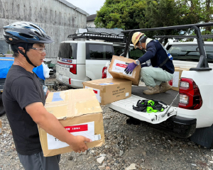 Volunteers unloading and carrying relief supplies from a vehicle.