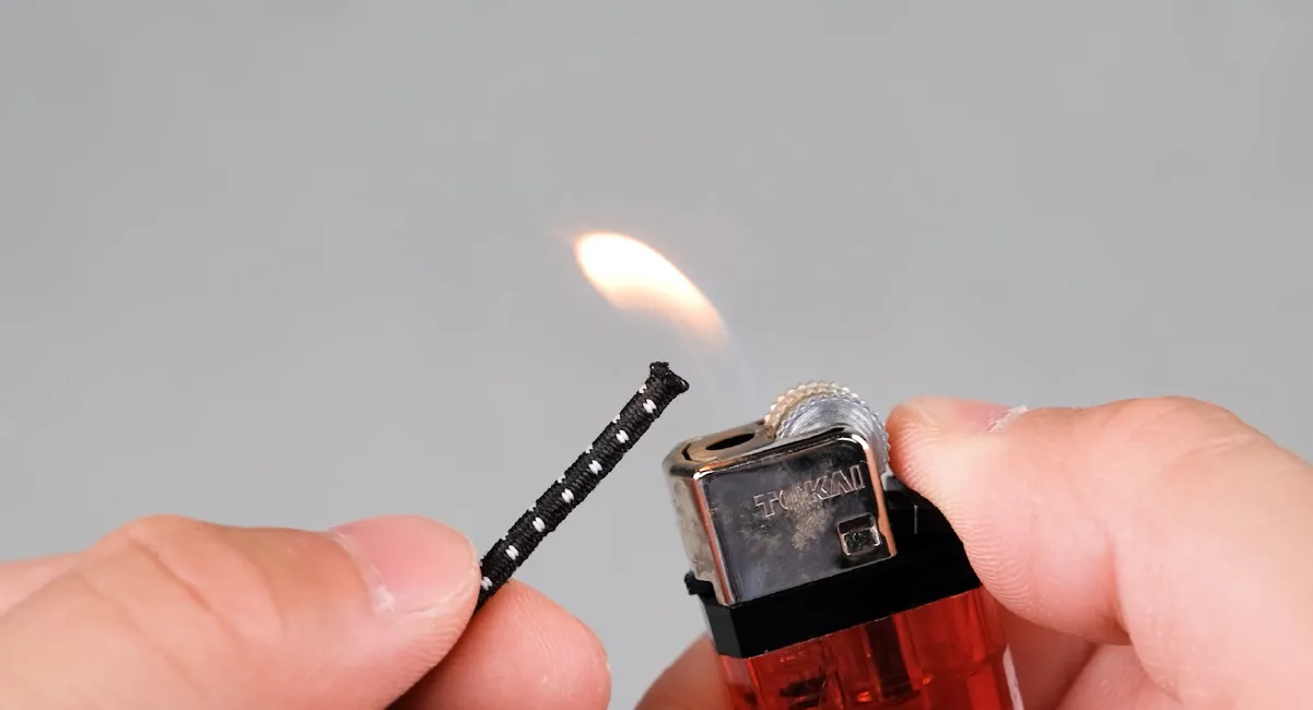 The cut end of the shock cord is being heated with a lighter.
