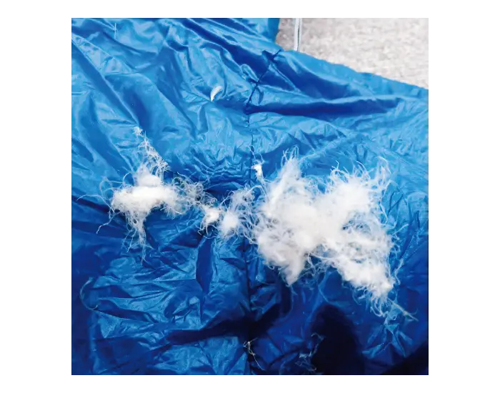 Sleeping bag before repair: Large holes due to heat-induced melting, with down feathers protruding.
