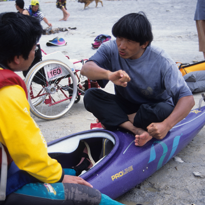 Isamu Tatsuno demonstrating kayaking technique and teaching a person in a wheelchair how to paddle.