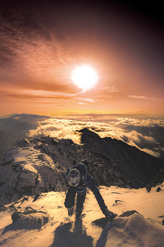 A mountaineer walking through snowy mountains with the sun at their back