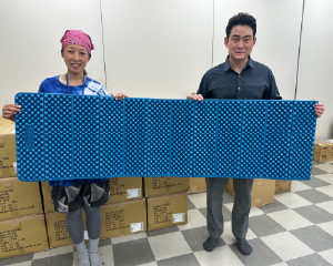 Mr. Noguchi and a woman holding an unfolded mat together.