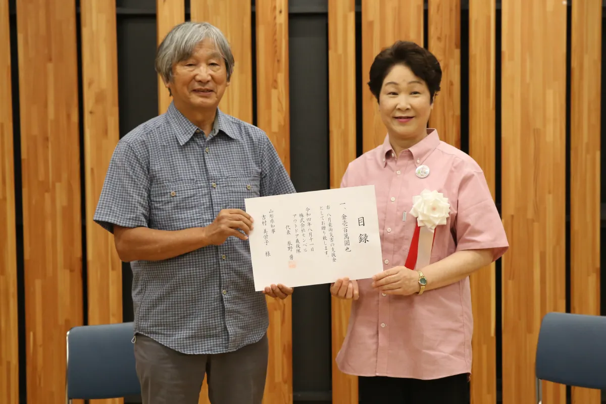 Isamu Tatsuno, representative of the Outdoor Gientai, presents a donation to Mieko Yoshimura, Governor of Yamagata Prefecture