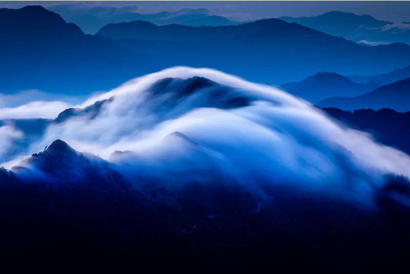 A massive amount of clouds flowing over the dark mountain ridges.