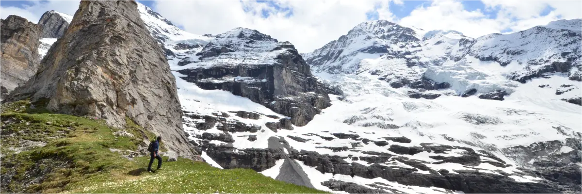 A lone climber gazes up at a snow-covered rock face.