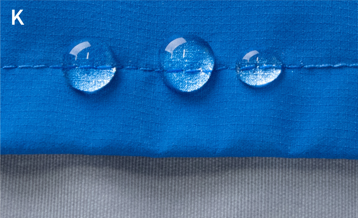 Water droplets are clinging to the seams, but they are not soaking in; the fabric is repelling water, leaving them as droplets.