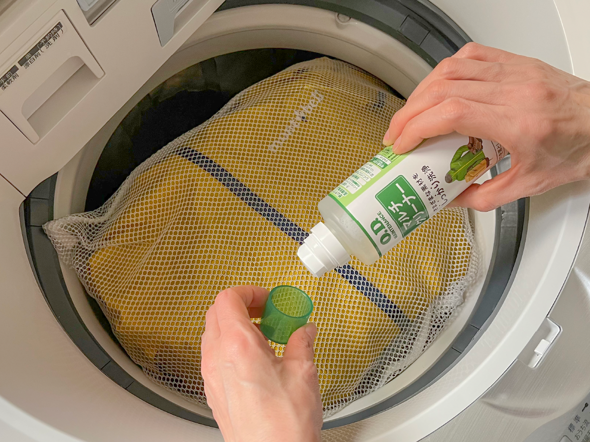 A photo of putting rainwear in a laundry net with multi-cleaner into a washing machine