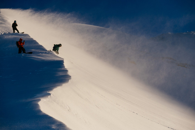 Three skiers and snowboarders attempting to descend a steep snowy slope