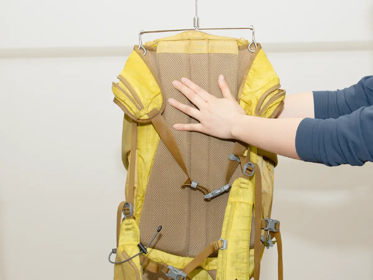 Photo of a backpack hanging upside down and squeezing water out of it by holding it by hand.